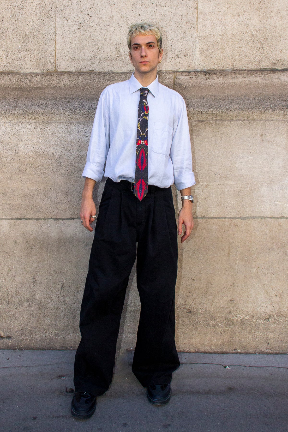 Homme vu de face portant la cravate NIELS avec une chemise bleu clair et un pantalon noir ample.