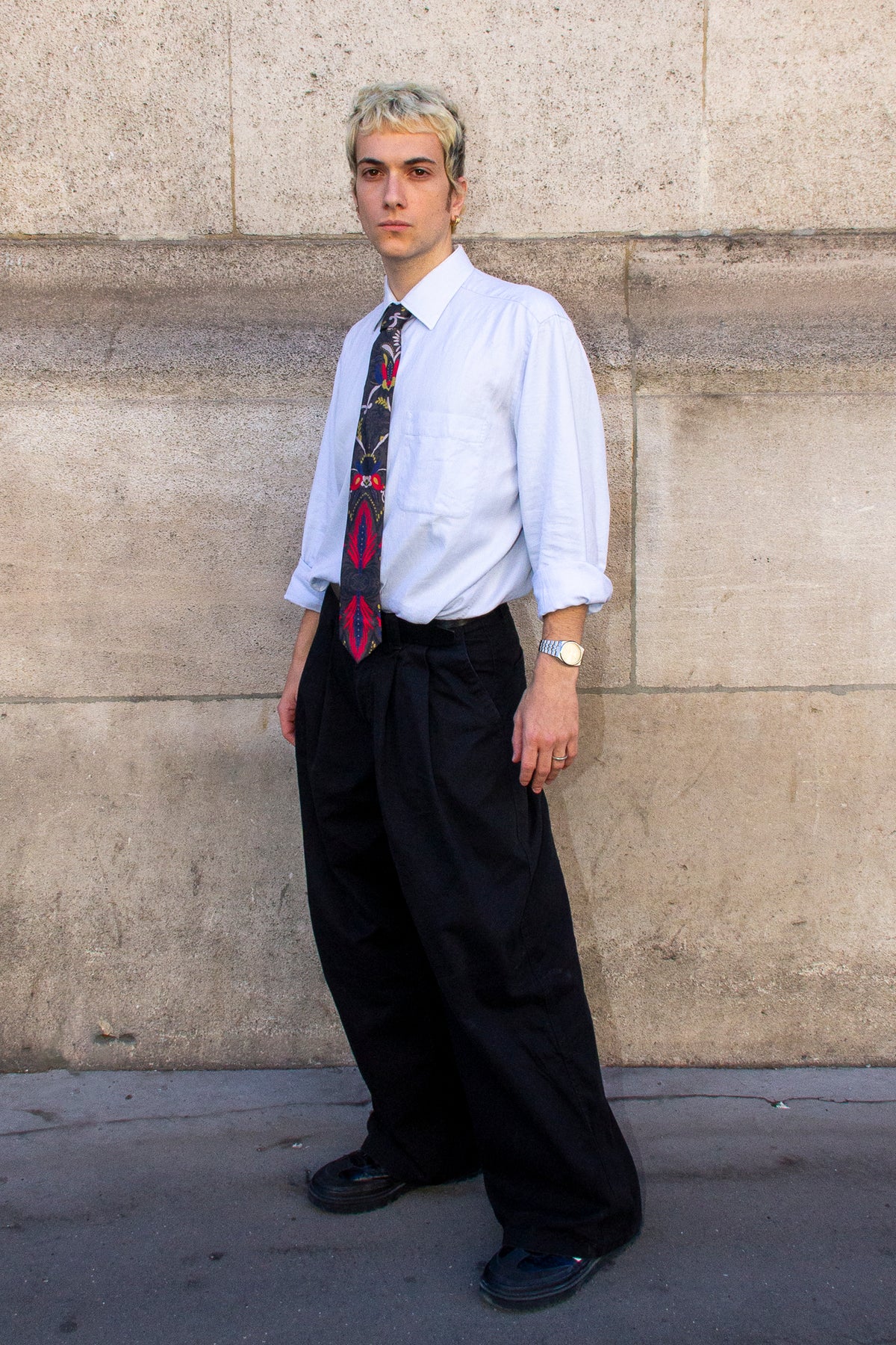 Homme de trois quarts portant la cravate NIELS avec une chemise bleu clair et un pantalon noir.
