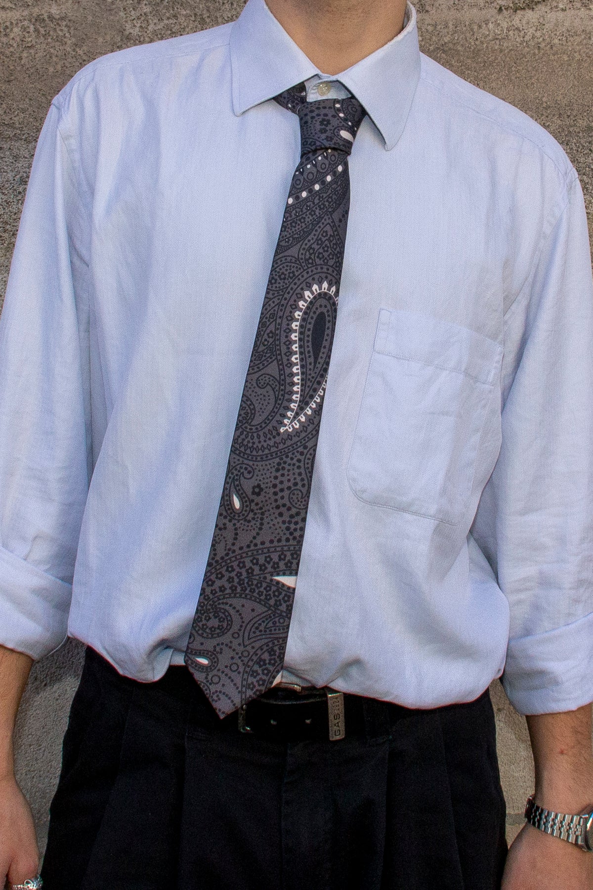 Gros plan sur la cravate en soie à motifs paisley gris ardoise portée avec une chemise bleu clair.