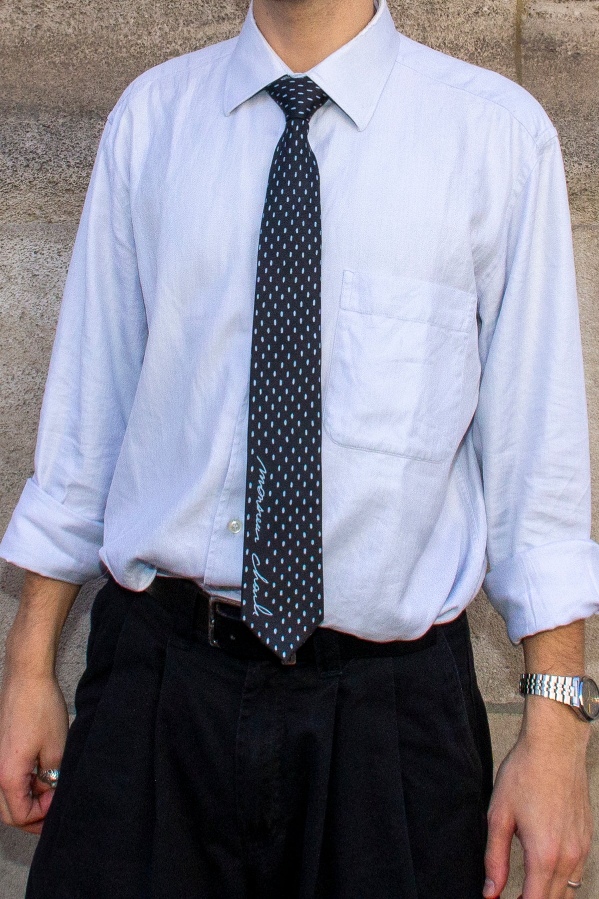 Gros plan sur la cravate en soie noire à petits pois blancs nouée sur une chemise bleu clair.