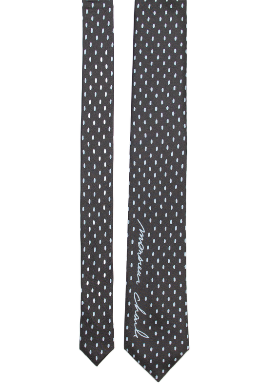 Cravate en soie noire à petits pois blancs et signature Monsieur Charli, les deux pans présentés à plat.