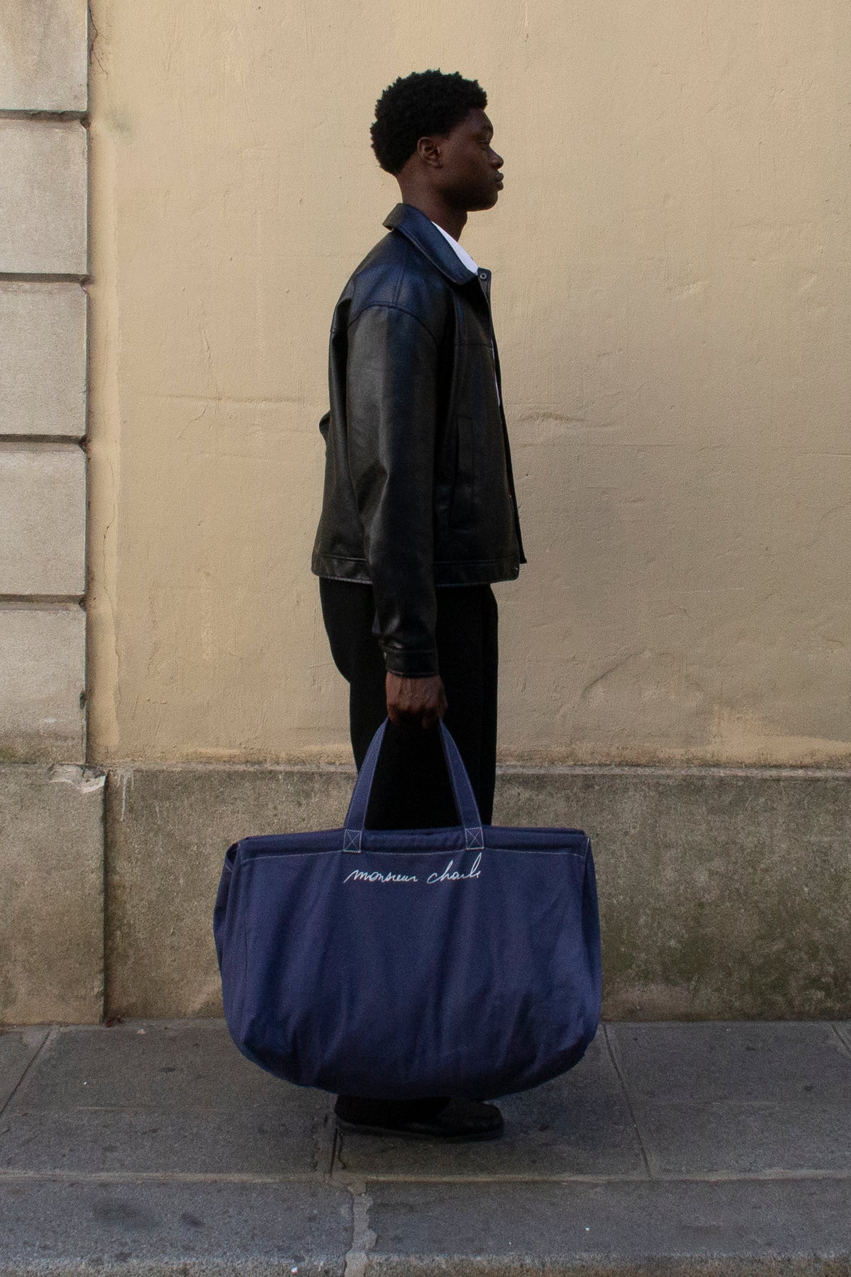 Homme de profil portant le maxi cabas bleu WALTER à la main devant un mur beige