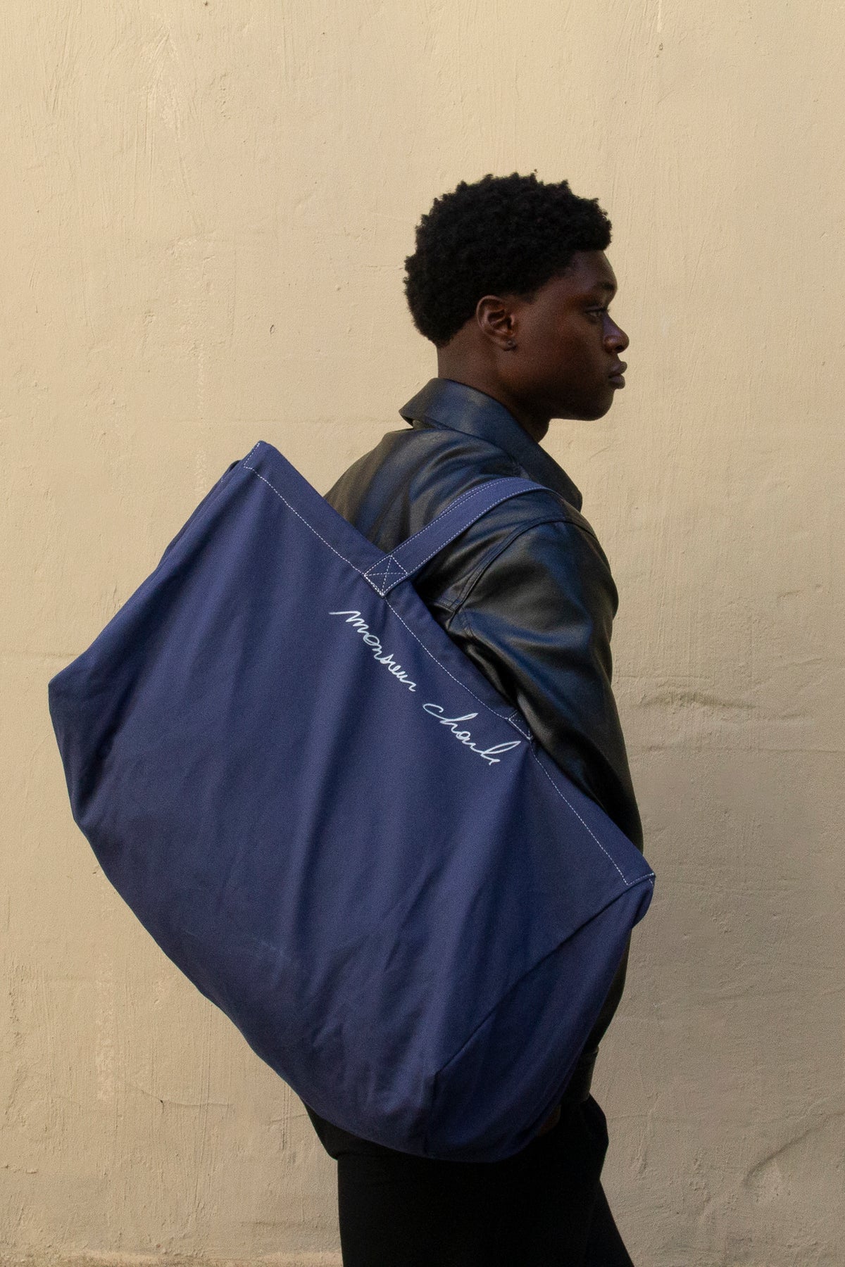 Homme de profil portant le maxi cabas bleu WALTER à la main devant un mur beige