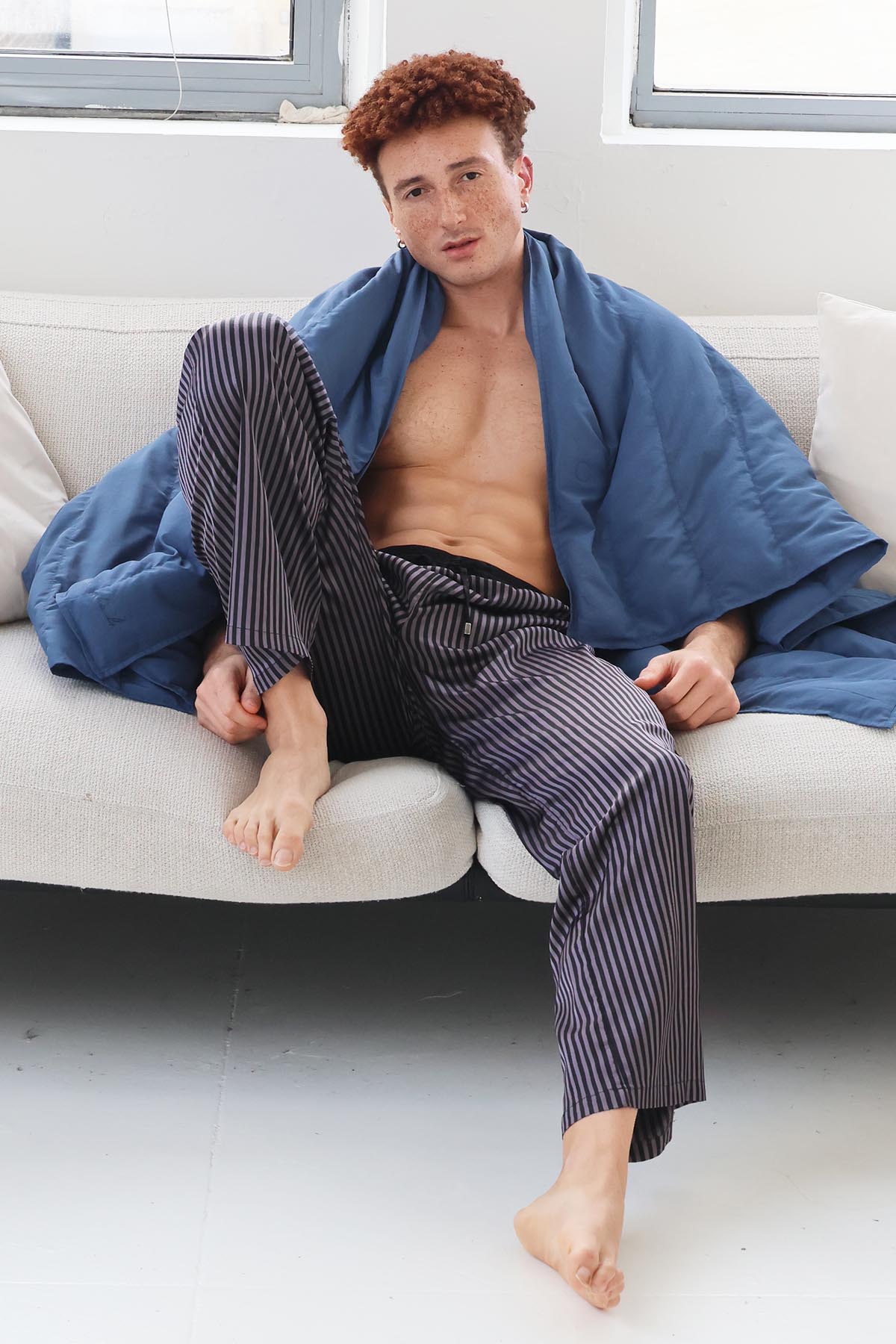 Un homme assis sur un canapé qui porte un plaid signé Monsieur Charli